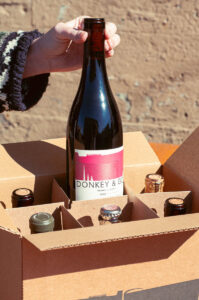 A staff member pulling a bottle of wine from a box holding 5 other bottles