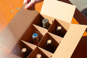 Staff members hand holding edge of box containing six bottles of wine
