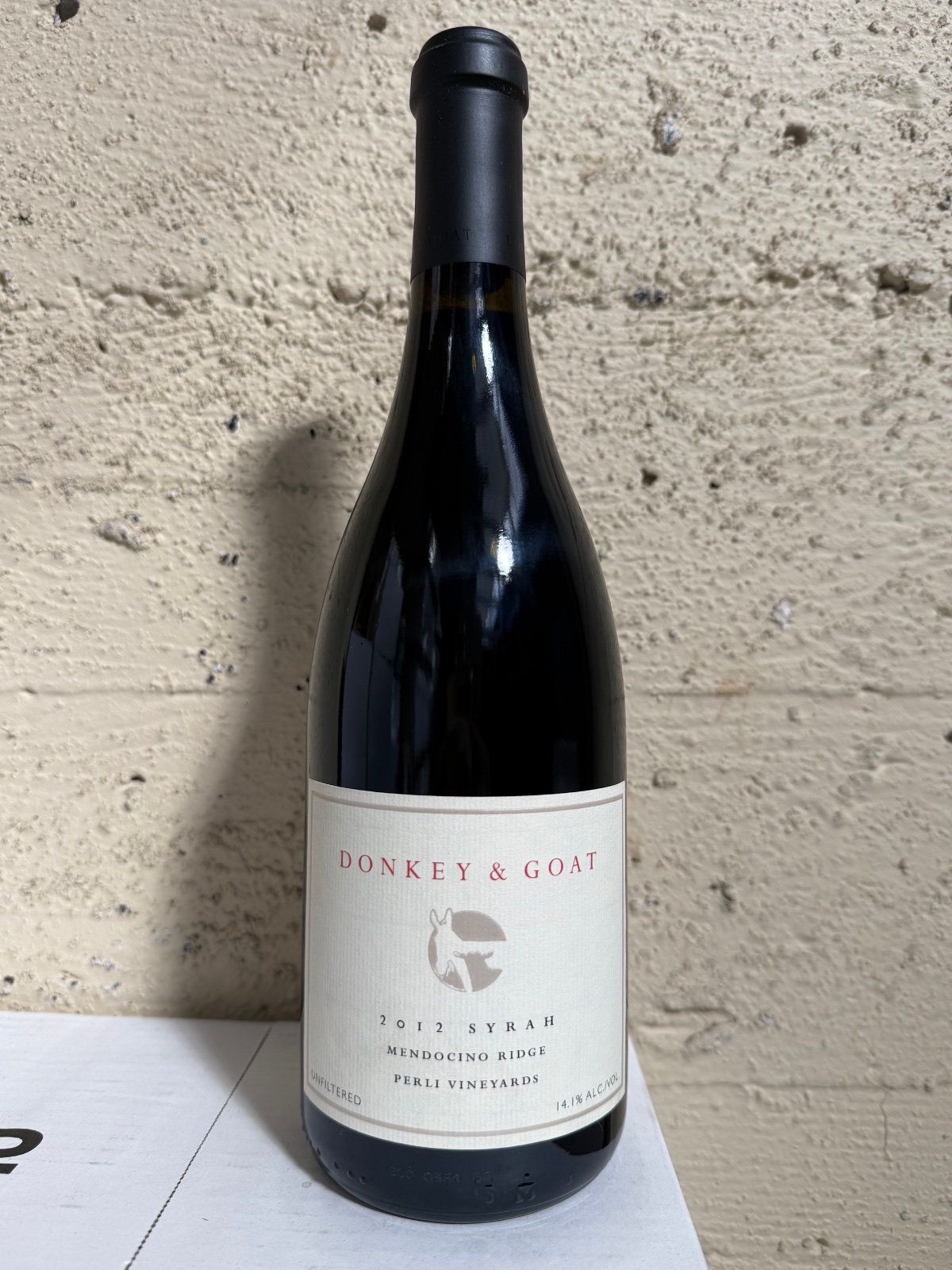 A bottle of 2012 Perli Syrah against the winery's concrete wall